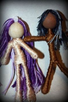 two handmade dolls standing next to each other on a white surface and one has purple hair