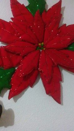 a red poinsettia with green leaves hanging on the wall in front of a white wall