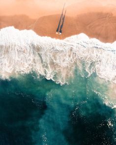 an aerial view of the ocean and beach with two sailboats in the water, from above