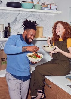 a man and woman eating food together in the kitchen