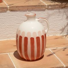 an orange and white striped vase sitting on the ground next to a wall with potted plants in it