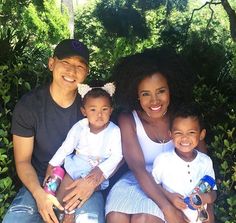 a man, woman and two children sitting on a bench in front of some bushes