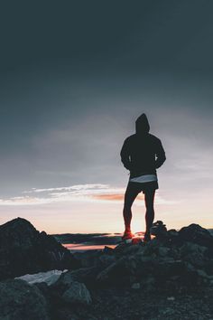 a man standing on top of a rocky beach next to the ocean at sunset or dawn