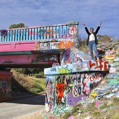 a man standing on the edge of a graffiti covered bridge with his arms in the air