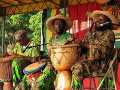 three men sitting on chairs playing musical instruments and drums in front of a tent with red curtains