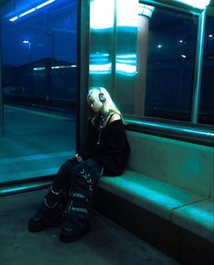 a woman with headphones sitting on a bench in front of a glass window at night