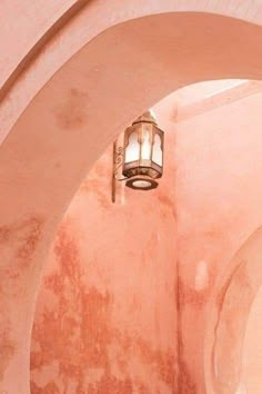 a light hanging from the side of a wall in a room with pink walls and arches