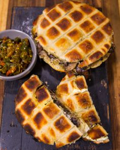 two waffle sandwiches cut in half on a cutting board next to a bowl of salsa