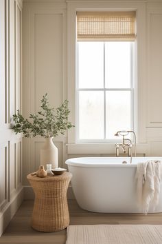 a white bath tub sitting under a window next to a wooden table with a vase on it