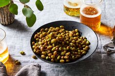 there is a bowl full of green beans next to some beer glasses and a potted plant