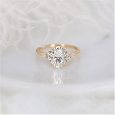 an engagement ring with three stones on it, sitting on a white surface in front of some feathers