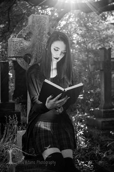 a woman sitting on a grave reading a book in front of a cross and sunbeam