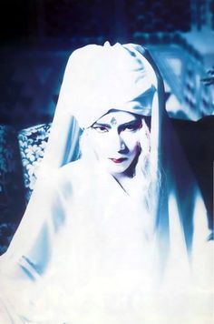 a woman dressed in white sitting on a chair with her head covered by a veil