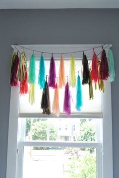 colorful tissue tassels hanging from a window sill in front of a white wall