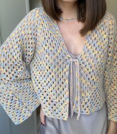 a woman is wearing a crocheted cardigan and posing for the camera with her hands on her hips