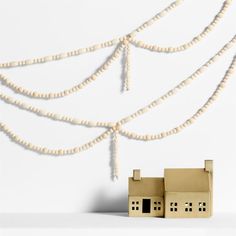 a wooden house next to a string of beads on a white wall with a tree in the background