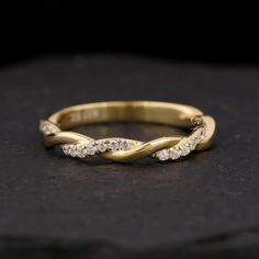 a yellow gold wedding band with diamonds on black stone background, close - up view