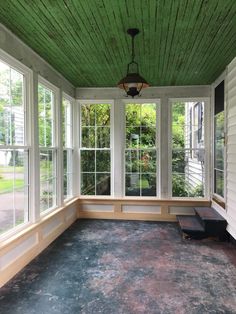 an empty sun room with green painted ceiling and white trim on the windows, along with two benches