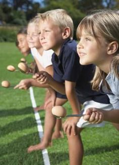 several children are lined up on the sidelines with eggs in their hands