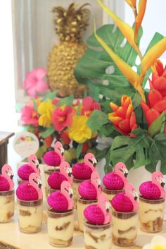 mini desserts with pink flamingos are on a table in front of tropical flowers