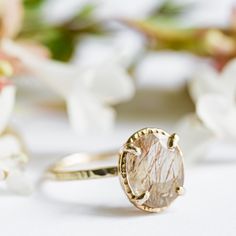 a close up of a ring on a white surface with flowers in the back ground