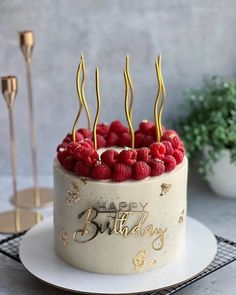 a birthday cake with raspberries on top and gold writing that says happy birthday