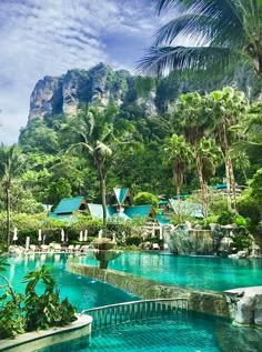 an outdoor swimming pool surrounded by lush green trees and mountain in the background with blue sky