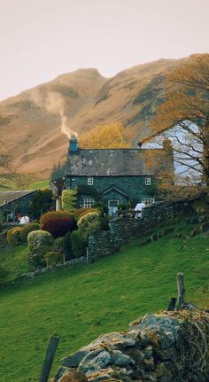 a house in the middle of a lush green field with mountains in the back ground