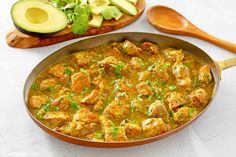 a pan filled with meat and vegetables on top of a table next to sliced avocado