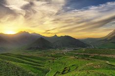 the sun is setting over some mountains and valleys with green grass on each side, while clouds are in the sky