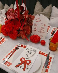 the table is set with red flowers and place settings