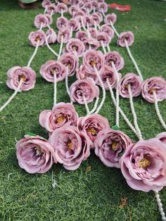 some pink flowers are on the grass and tied together with twine strings to make it look like they have been made out of paper