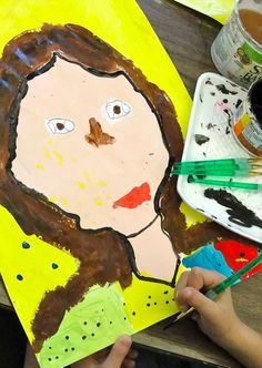 a child's hand is holding paint and painting on a piece of paper that has a drawing of a woman