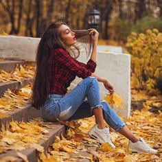 a beautiful young woman sitting on top of steps covered in leaves and looking up at the sky