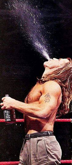 a man with long hair spraying water on his face while standing next to a boxing ring