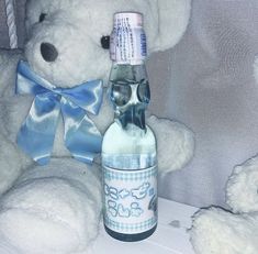 a white teddy bear sitting next to a bottle with a blue bow on it's neck