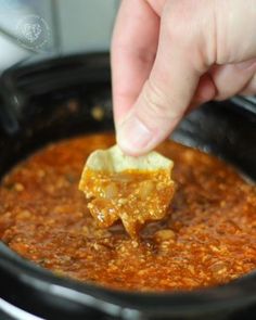 a person dipping some food into a crock pot filled with chili and cheese sauce