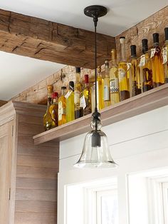 bottles of liquor are lined up on the shelf above the kitchen sink in this rustic home