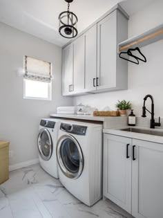 a washer and dryer in a white laundry room with marble counter tops, cabinets, and drawers