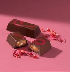 three pieces of chocolate sitting on top of a pink surface next to candy and candies