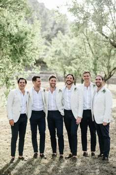 a group of men standing next to each other wearing white suits and bow ties in front of trees