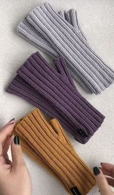 four different colored knitted mittens sitting on top of a white table next to a woman's hand