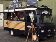 a black food truck parked in front of a building with a surfboard on the roof