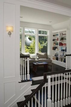 a living room filled with furniture and bookshelves next to a stair case in front of a window