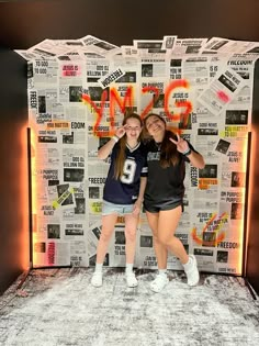 two girls standing in front of a wall covered with newspaper