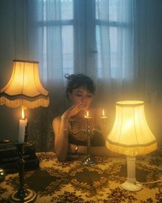 a woman sitting at a table in front of two lamps with one light on it