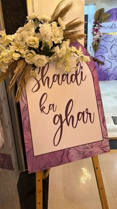 a sign that says shaadi and ghaar with flowers on it in front of a door