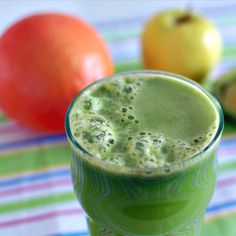 a green smoothie in a glass next to some fruit