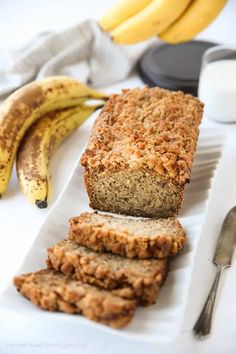 sliced banana bread sitting on top of a white plate next to two bananas and a glass of milk