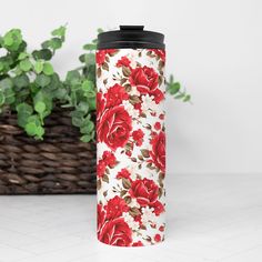 a red and white flowered travel mug next to a basket